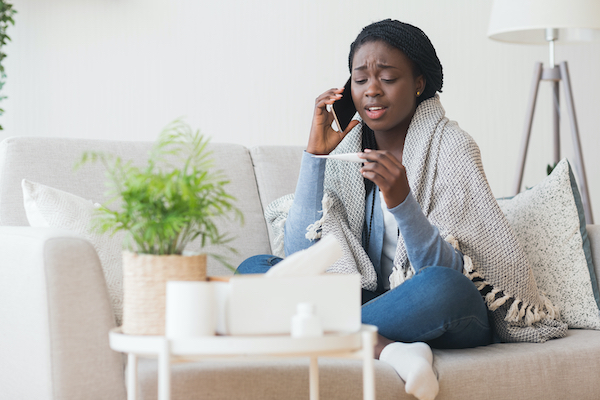 woman taking her temperature while talking on the phone